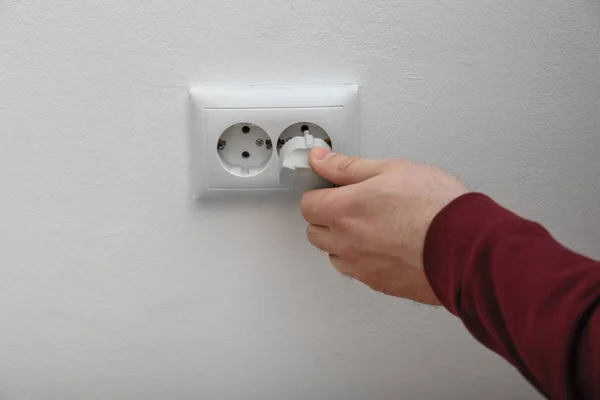 Electrician inserting plug into power socket on white background, closeup