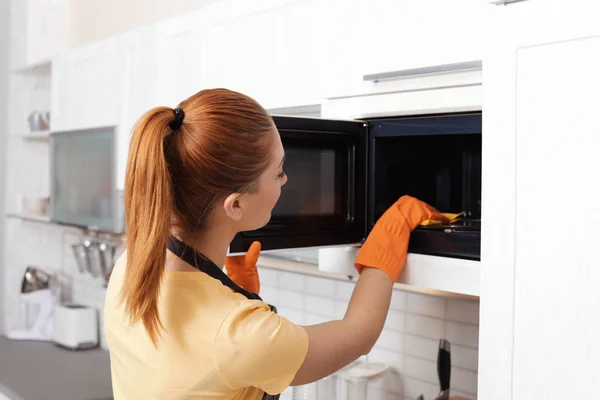 Mulher de limpeza forno de microondas com pano na cozinha — Fotografia de Stock