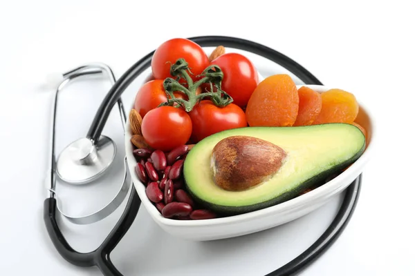 Herzförmige Schale mit gesunden Produkten und Stethoskop auf weißem Hintergrund — Stockfoto