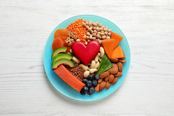 Plate with heart-healthy products on wooden background, top view