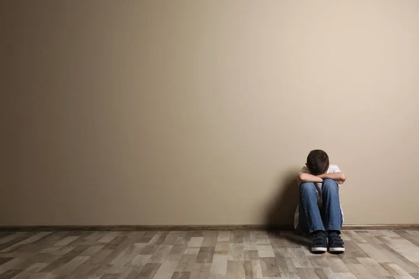 Αναστατωμένος αγόρι κάθεται στο πάτωμα στον τοίχο χρώμα. Χώρος για κείμενο — Φωτογραφία Αρχείου