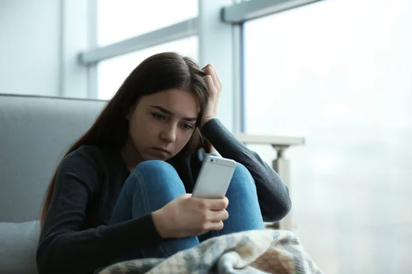 Menina adolescente perturbado com smartphone sentado na janela dentro de casa. Espaço para texto — Fotografia de Stock