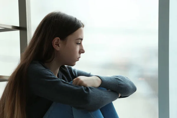 Upset teenage girl sitting at window indoors. Space for text — Stock Photo, Image