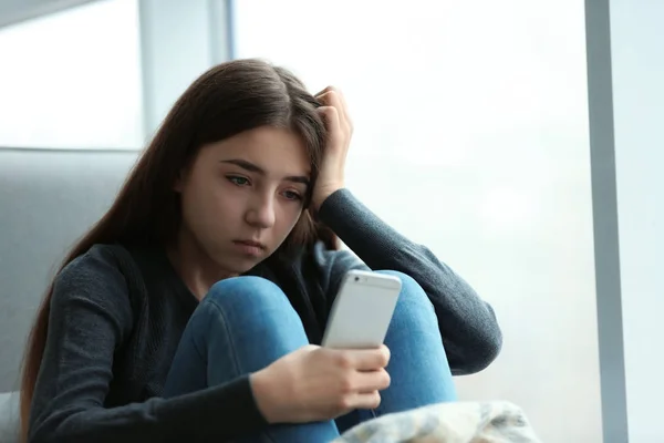 Menina adolescente perturbado com smartphone sentado na janela dentro de casa. Espaço para texto — Fotografia de Stock