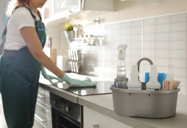 Bacia com suprimentos de limpeza na mesa e zelador profissional na cozinha — Fotografia de Stock