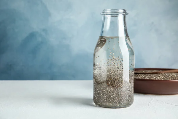 Composição com garrafa de água e sementes de chia na mesa contra fundo de cor, espaço para texto — Fotografia de Stock