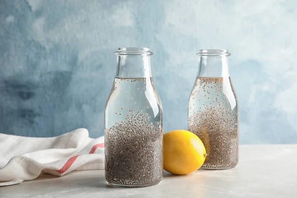 Composição com garrafas de água e sementes de chia na mesa contra fundo de cor — Fotografia de Stock