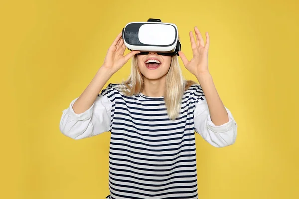 Mulher emocional jogando jogos de vídeo com fone de ouvido realidade virtual em fundo de cor — Fotografia de Stock