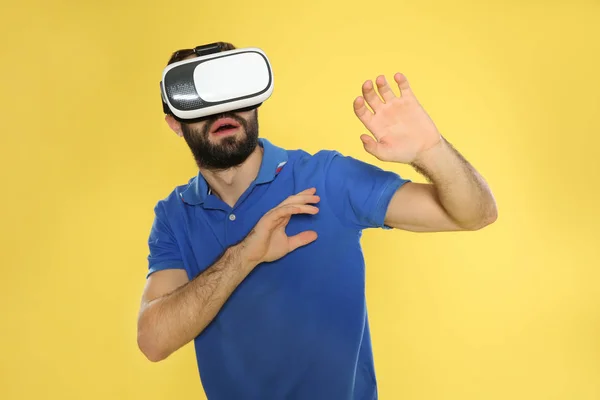 Jovem emocional jogando videogames com fone de ouvido de realidade virtual em fundo de cor — Fotografia de Stock