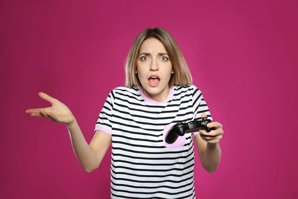 Mujer joven emocional jugando videojuegos con controlador en el fondo de color —  Fotos de Stock