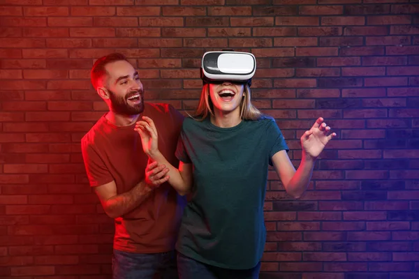 Mulher emocional jogando videogames com fone de ouvido VR e homem feliz perto da parede de tijolo — Fotografia de Stock