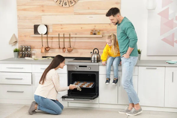 Mulher e sua família tirando bandeja com biscoitos cozidos do forno na cozinha — Fotografia de Stock