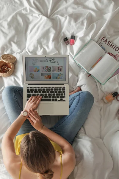 Frau und Laptop mit offenem Kochblog auf dem Bett, Draufsicht — Stockfoto