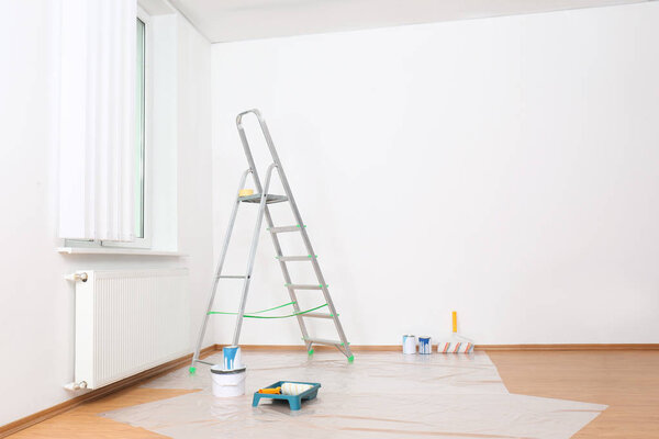 Лестница и инструменты для покраски у стены в пустой комнате