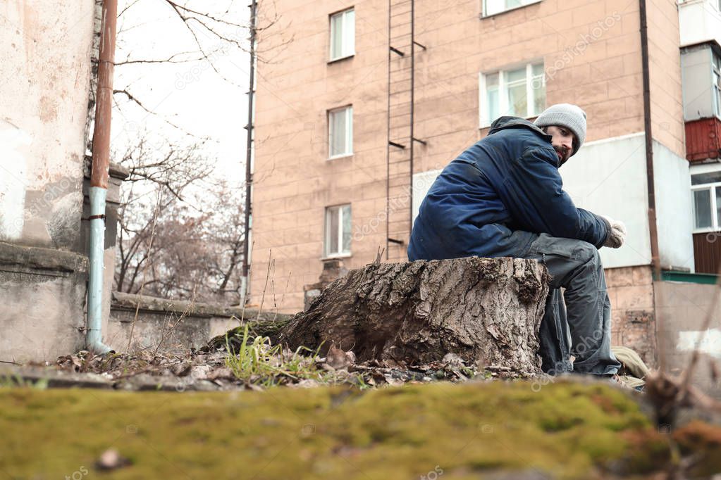Poor homeless man sitting on stump outdoors