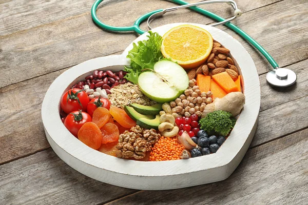 Plateau en forme de coeur avec des produits sains et stéthoscope sur fond en bois — Photo