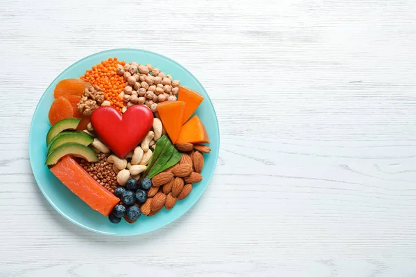 Plate with heart-healthy products on wooden background, top view. Space for text