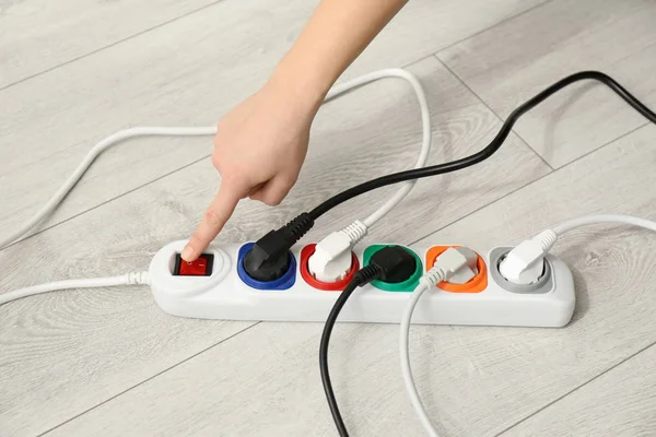 Woman pressing power button of extension cord on floor, closeup. Electrician's professional equipment