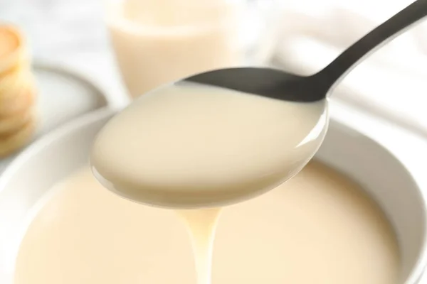 Spoon of pouring condensed milk over bowl, closeup. Dairy products — Stock Photo, Image