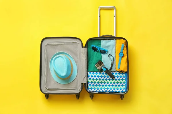 Offener Koffer mit Sommerkleidung und Accessoires auf farbigem Hintergrund, Ansicht von oben — Stockfoto