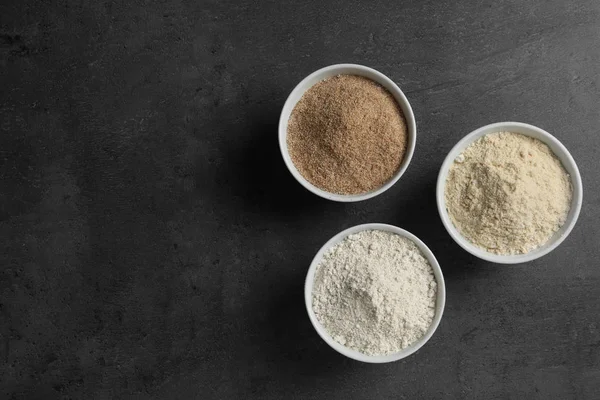 Tigelas com diferentes tipos de farinha no fundo cinza, vista superior. Espaço para texto — Fotografia de Stock