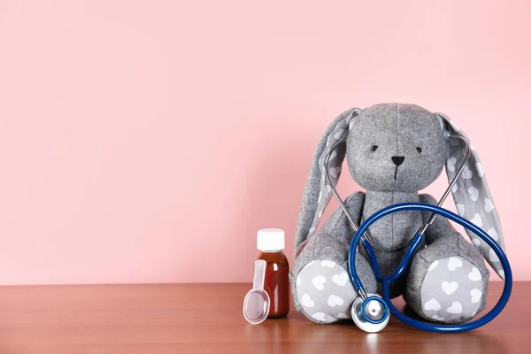 Leksaks kanin med stetoskop och Host medicin på bordet mot färg bakgrund, utrymme för text. Barn sjukhuset — Stockfoto