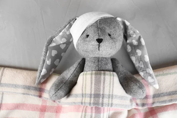 Conejito de juguete con vendaje acostado debajo de la manta sobre fondo gris, vista superior. Hospital de niños — Foto de Stock