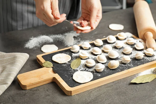 Женщина готовит вкусные пельмени над серым столом, крупным планом — стоковое фото