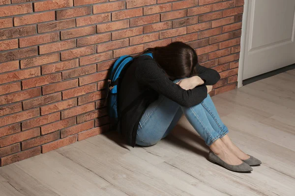 Upprörd tonårs flicka med ryggsäck sitter på golvet nära väggen. Utrymme för text — Stockfoto