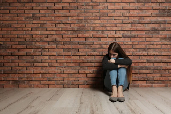 Upset teenage girl sitting on floor near wall. Space for text — Stock Photo, Image