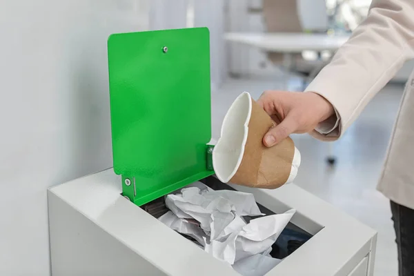 Γυναίκα που βάζει μεταχειρισμένο χάρτινο κύπελλο σε κάδο σκουπιδιών στο μοντέρνο γραφείο, κοντινά πλάνα. Ανακύκλωση αποβλήτων — Φωτογραφία Αρχείου