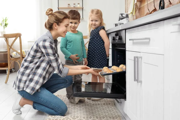 Мать и ее дети достают печенье из духовки на кухне — стоковое фото
