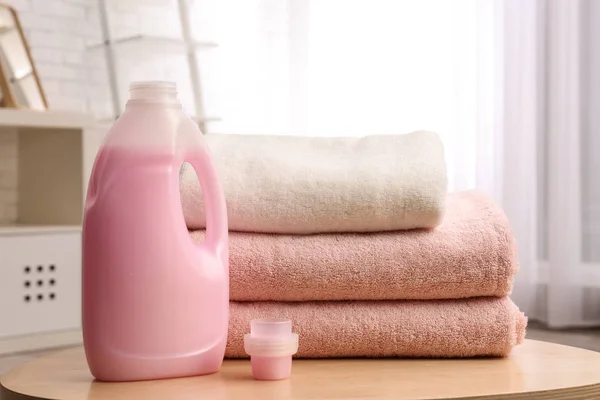 Garrafa de detergente e toalhas limpas na mesa dentro de casa. Dia de lavandaria — Fotografia de Stock