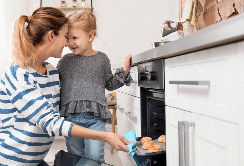 Mother and her daughter taking out cookies from oven in kitchen