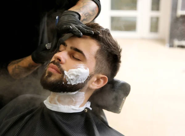 Профессиональный парикмахер бритья клиента с бритвой в парикмахерской — стоковое фото