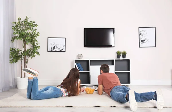 Giovane coppia sdraiata su tappeto e guardando la TV a casa — Foto Stock