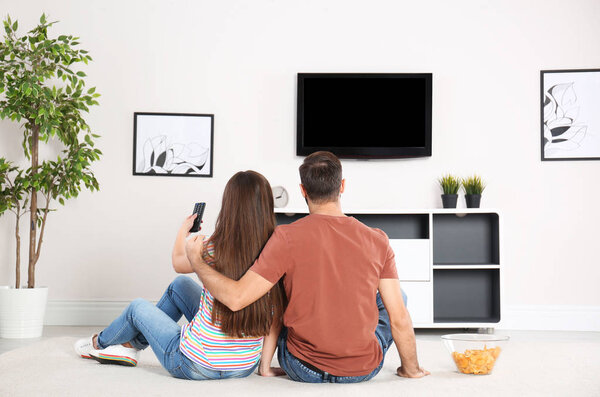 Young couple sitting on floor and watching TV at home
