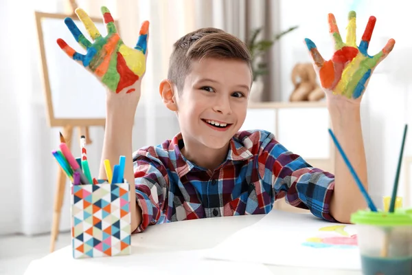 Klein kind met geverfde handen aan tafel binnenshuis — Stockfoto