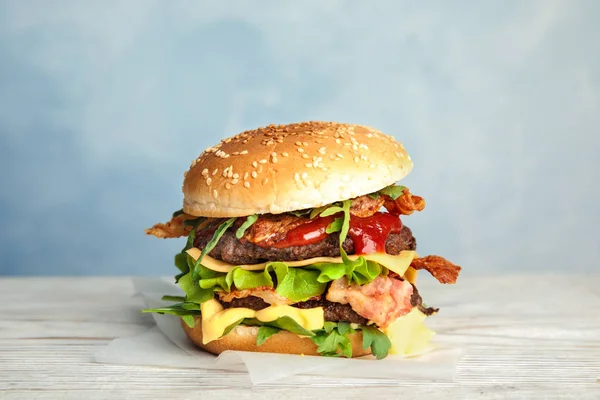 Chutné Burger se slaninou na stole proti barevnému pozadí — Stock fotografie