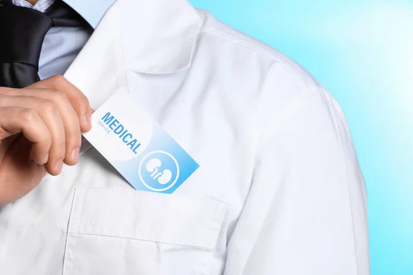 Doctor poniendo la tarjeta de visita en el bolsillo en el fondo de color, primer plano. Servicio médico — Foto de Stock