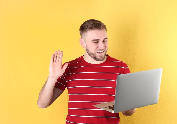 Jonge man met behulp van video-chat op laptop tegen kleur achtergrond — Stockfoto