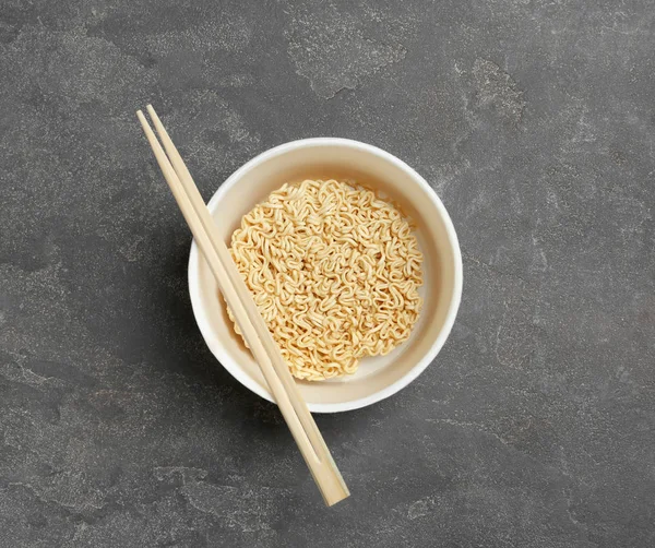 Copo de macarrão instantâneo com pauzinhos em fundo cinza, vista superior — Fotografia de Stock