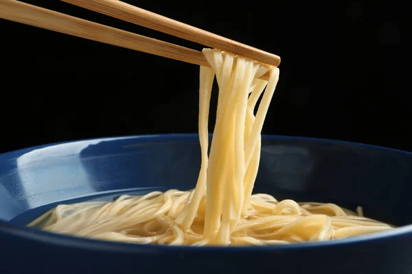 Comer macarrão com pauzinhos contra fundo preto, close-up — Fotografia de Stock