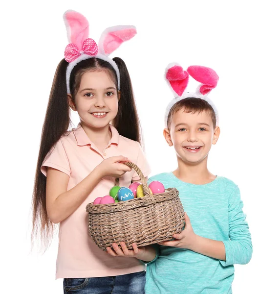 Cute children in bunny ears headbands holding basket with Easter eggs on white background — Stock Photo, Image