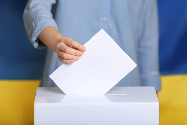 Woman putting voting paper into ballot box against Ukrainian flag, closeup — Stock Photo, Image