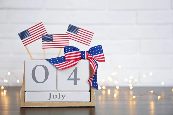 Calendario de madera con banderas de EE.UU. y arco en la mesa contra la pared de ladrillo, espacio para el texto. Feliz Día de la Independencia — Foto de Stock