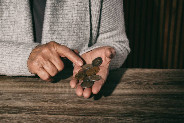 Poor senior woman with coins at table, closeup. Space for text