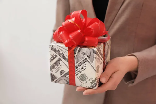 Mujer sosteniendo caja de regalo envuelta en dólares sobre fondo claro, primer plano — Foto de Stock