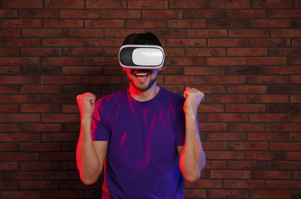 Emocjonalny człowiek grając w gry wideo z zestawu słuchawkowego wirtualnej rzeczywistości w pobliżu muru ceglanego — Zdjęcie stockowe