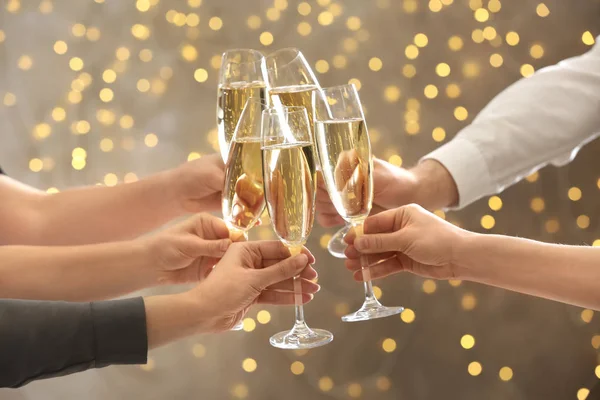 People clinking glasses with champagne against blurred lights, closeup. Bokeh effect